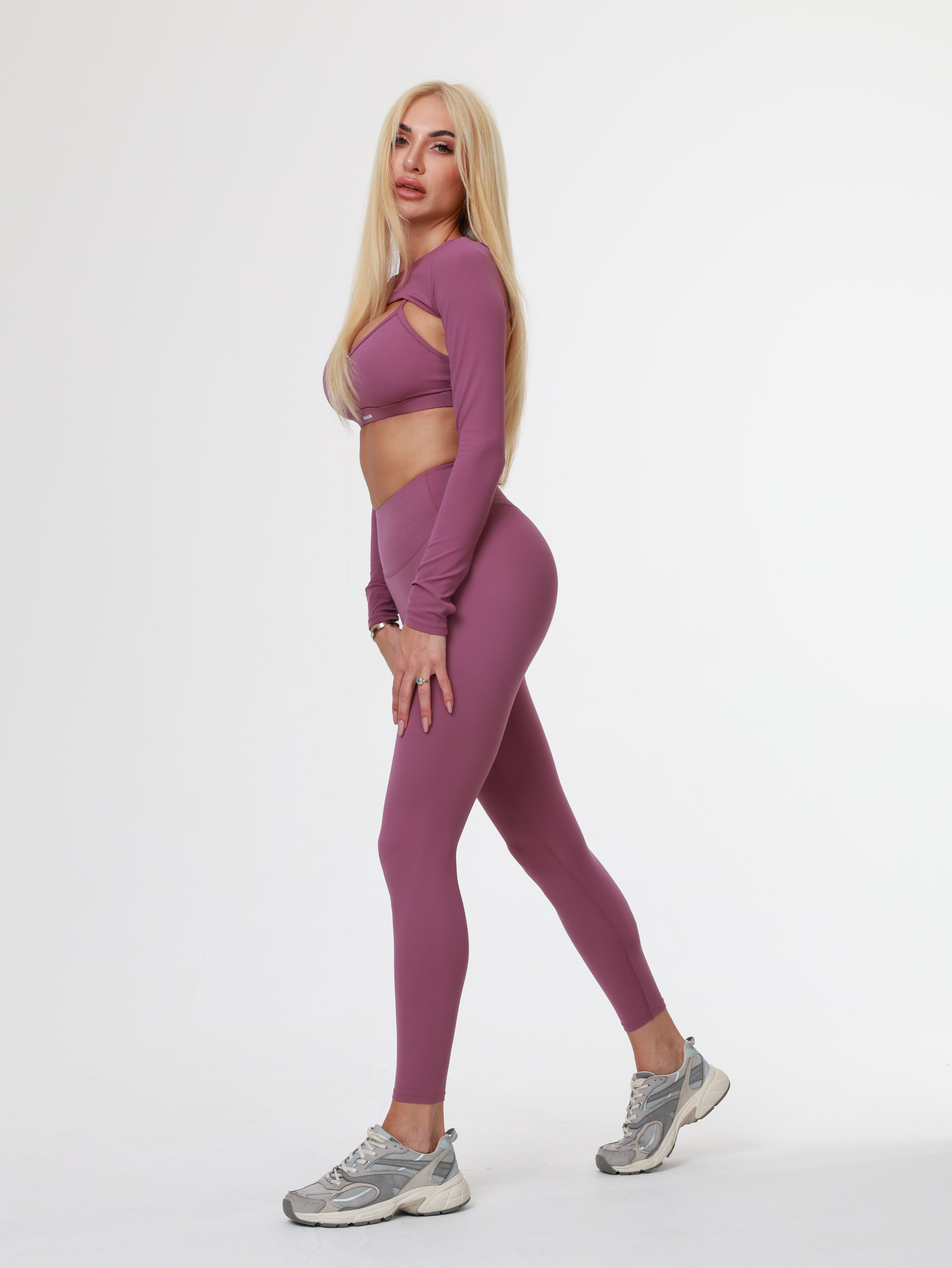 Person in purple Amethyst Leggings , bra and long sleeve top wear lying on a white background