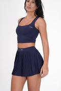 Woman wearing a navy Solrise' Top and pleated skirt with 'Balenciaga' branding on a white background