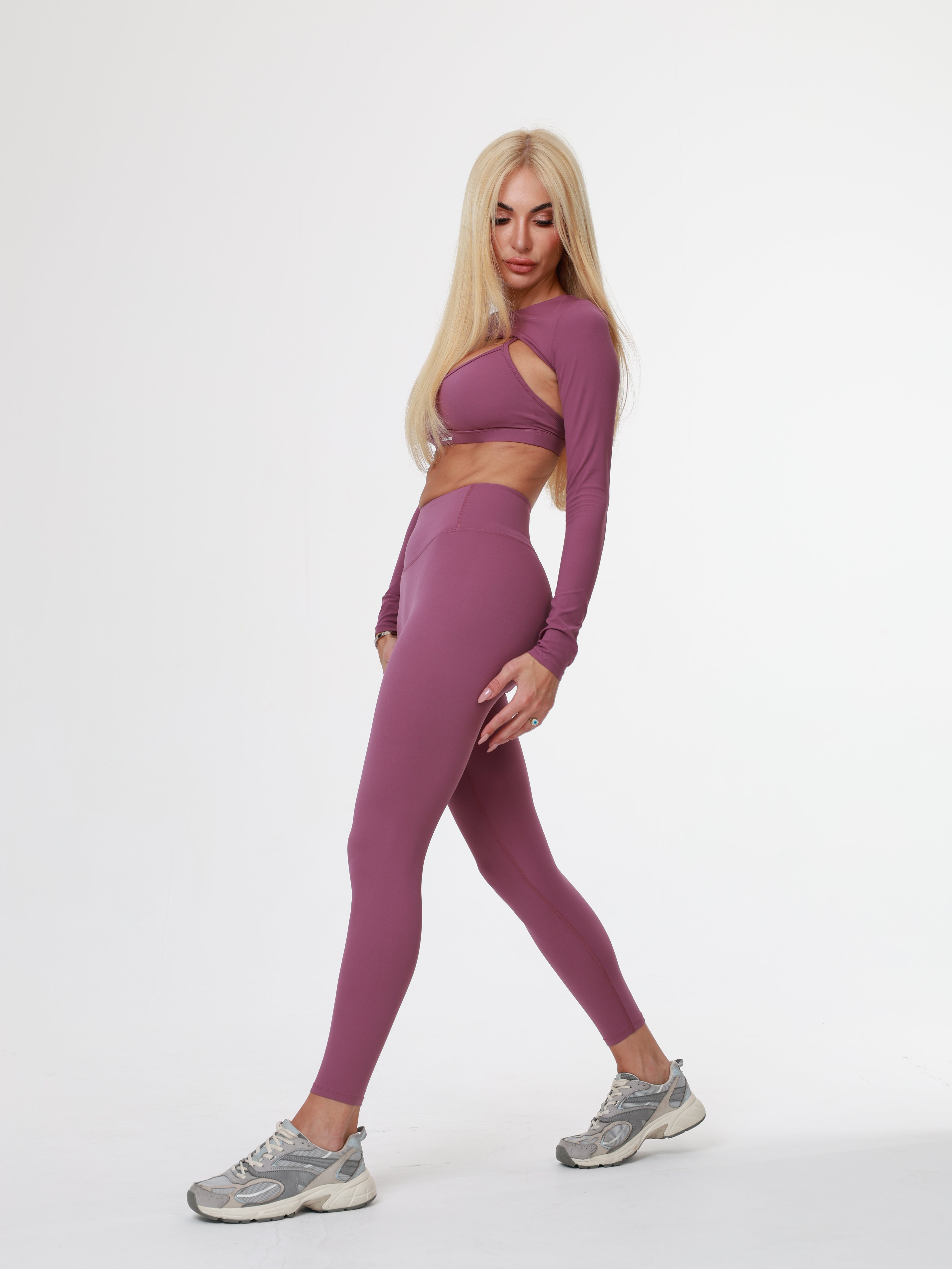 Woman in purple Amethyst Leggings , bra and long sleeve top wear posing on a white background