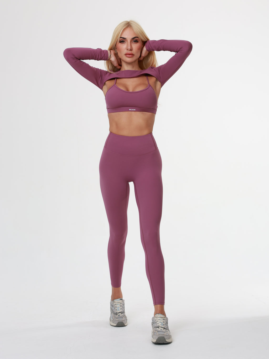 Woman in purple Amethyst Leggings , bra and long sleeve top wear lying on a white background