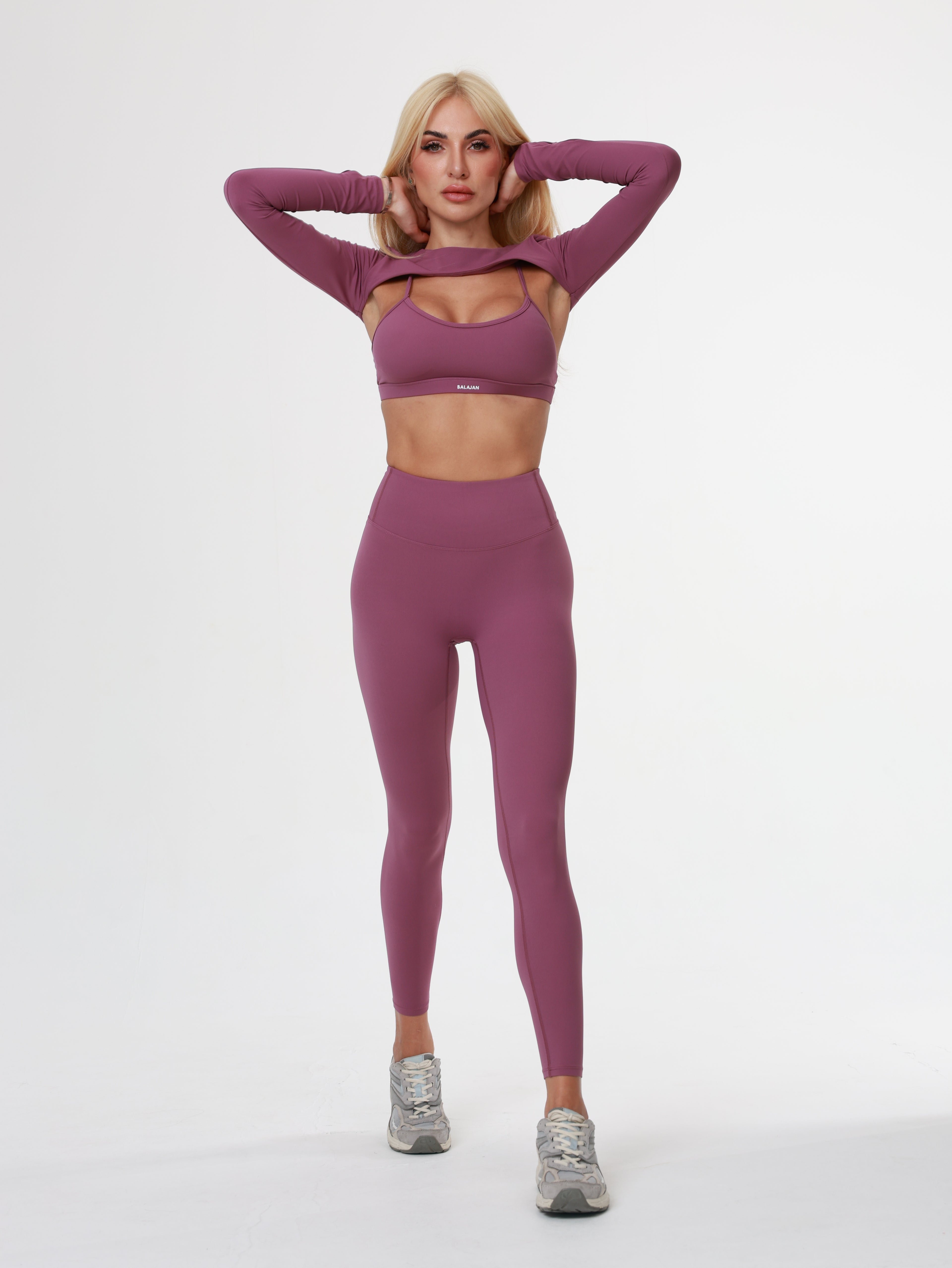 Woman in purple Amethyst Leggings , bra and long sleeve top wear lying on a white background