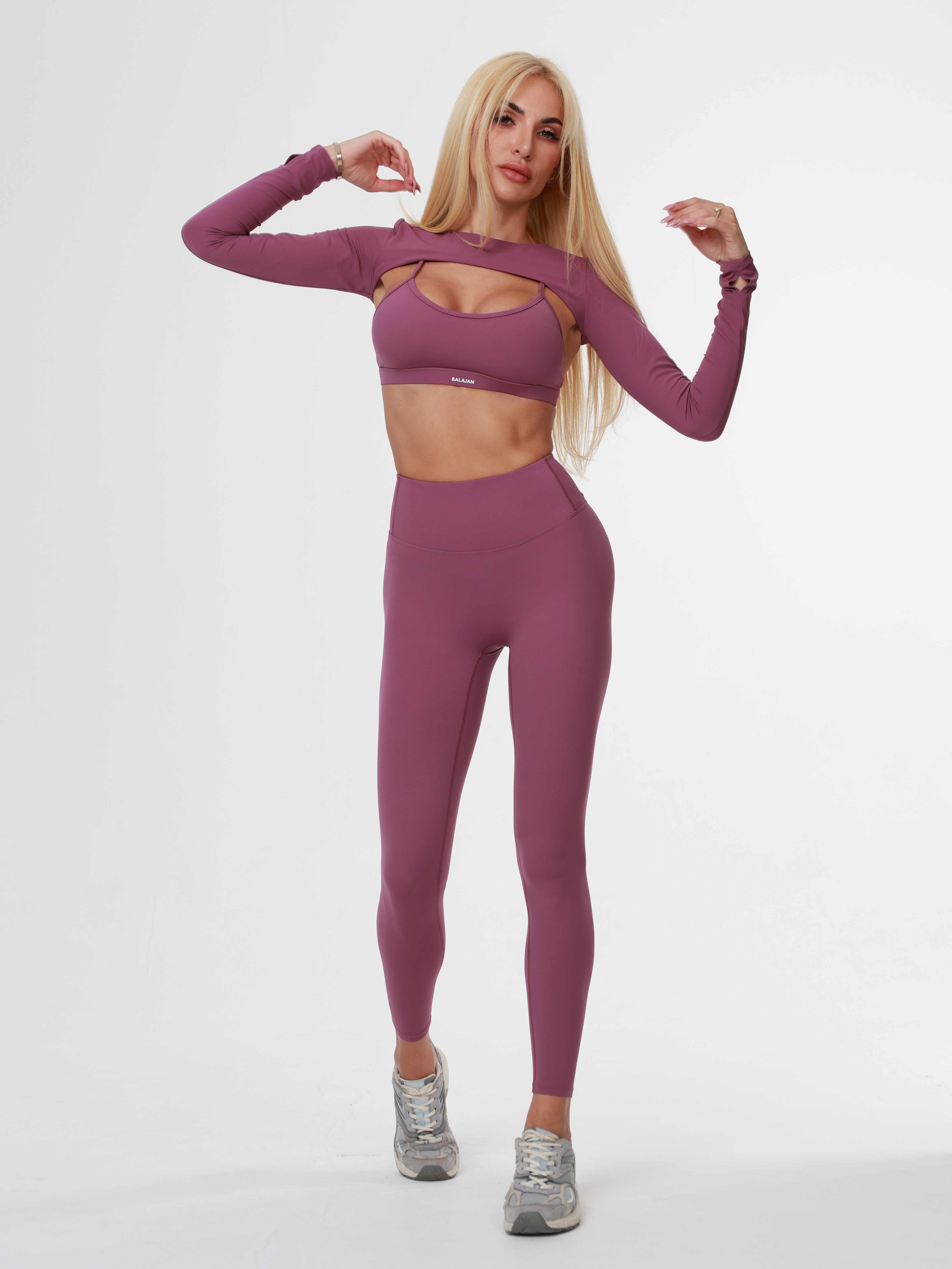 Woman wearing a purple athletic Amethyst Leggings , bra and long sleeve top on a white background