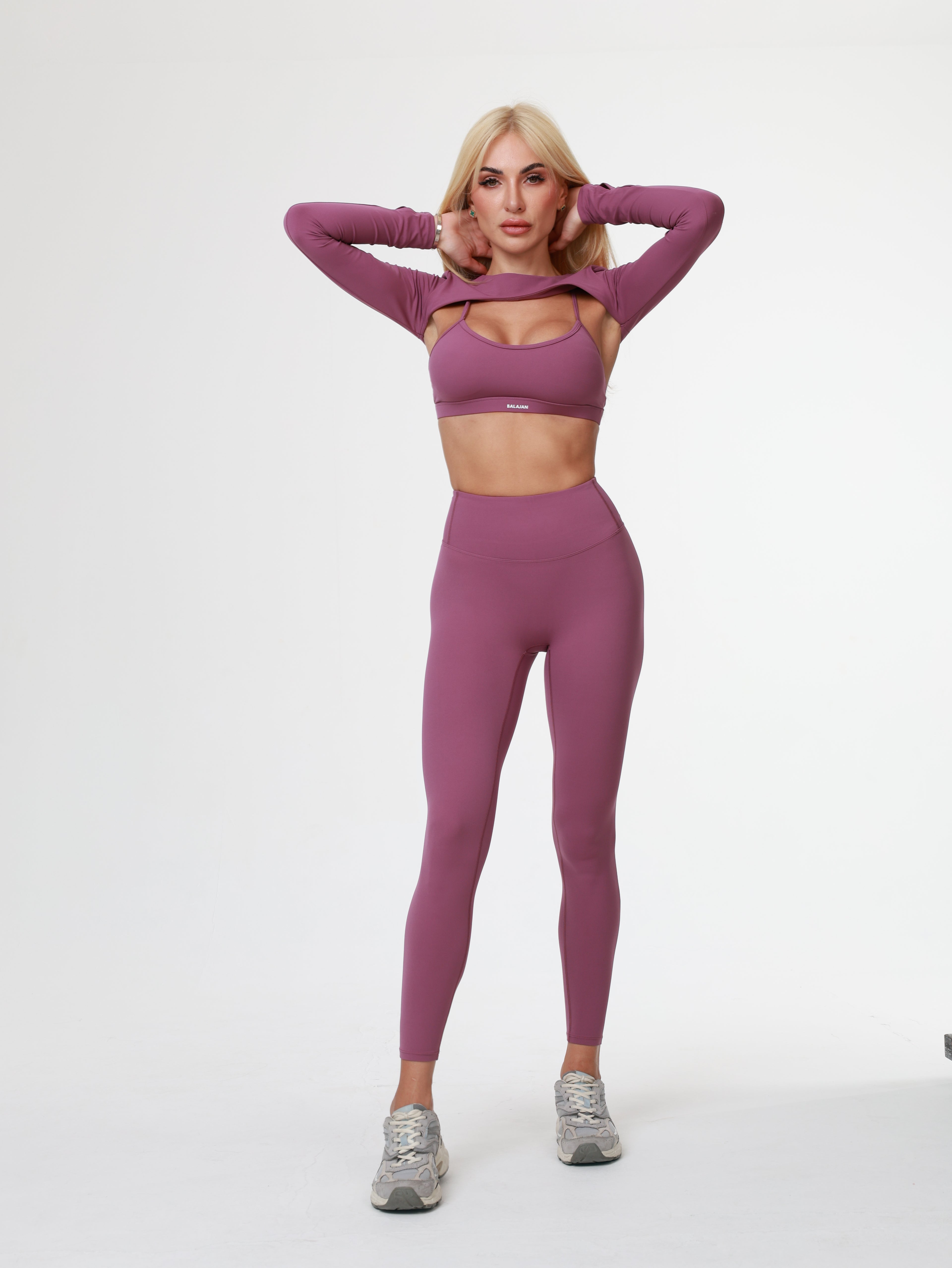 Woman in purple Amethyst Leggings , bra and long sleeve top wear lying on a white background