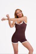 Woman wearing a brown activewear Palm Flex One Piece' bodysuit with white trim on a white background