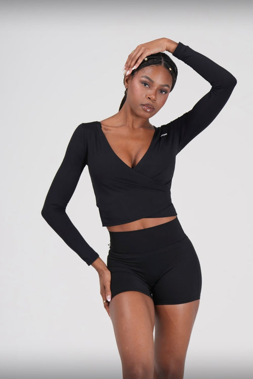 Woman wearing a black long-sleeve Bay Breeze Wrap Top' and shorts on a light gray background