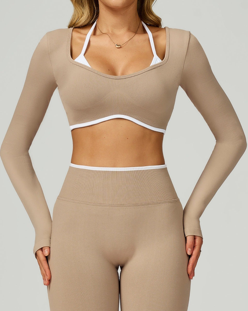Person wearing a beige long-sleeve athletic top and leggings on a plain background