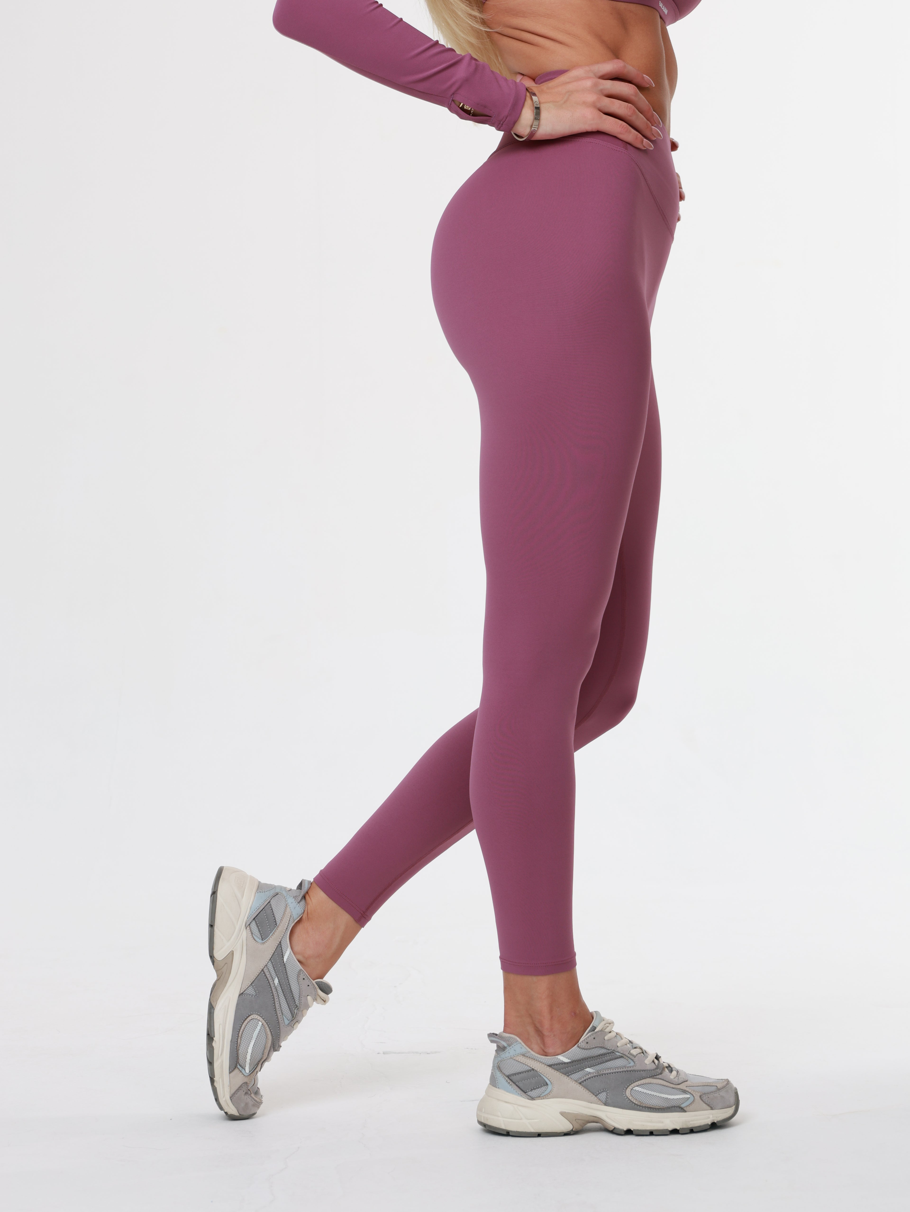Person wearing purple Amethyst Leggings , bra and long sleeve top and gray sneakers against a white background